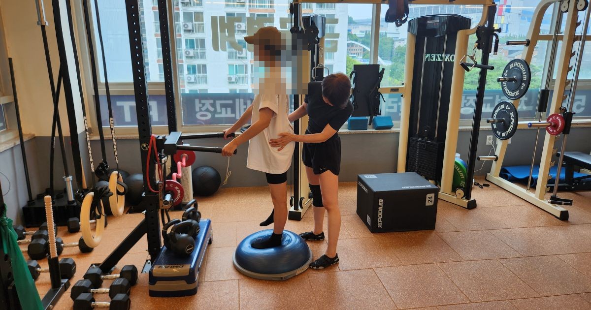 보수볼 위에서 균형을 잡으며 트레이너가 골반을 잡아주는 1:1 교정 운동